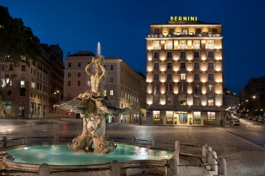 View from outside of the beautifully illuminated Sina Bernini Bristol Hotel and Triton Fountain in the evening.