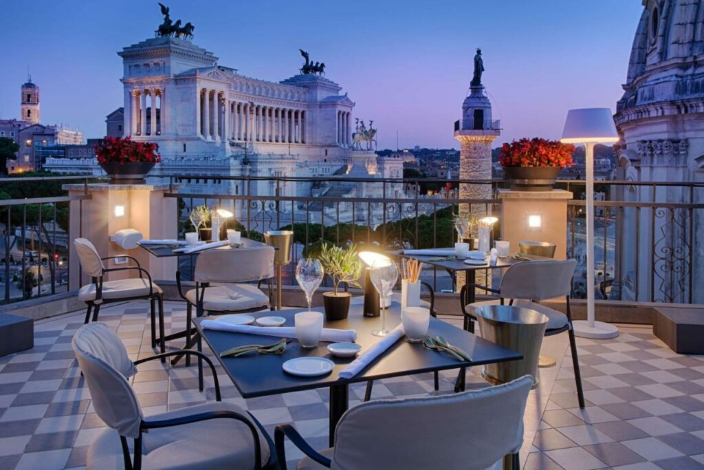 Rooftop terrace bar and restaurant of The NH Collection Roma Fori Imperiali Hotel with stunning views of the Roman Forum, in the sunset.