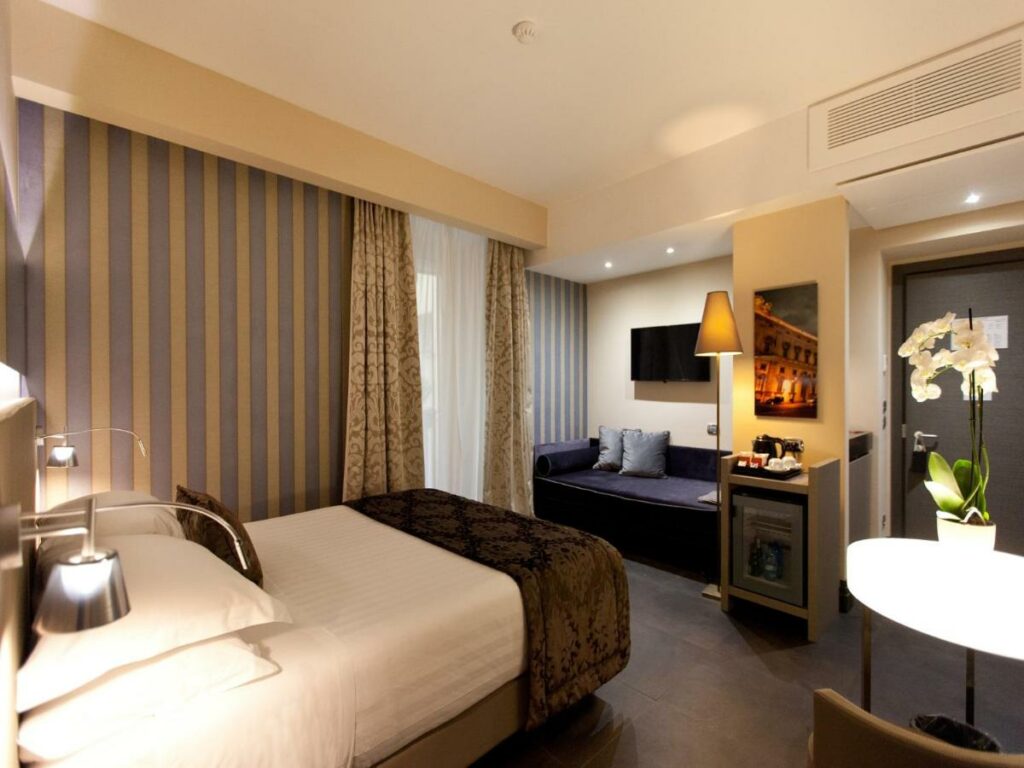 A nicely decorated hotel room with a double bed, sofa, lamp, and flowers.