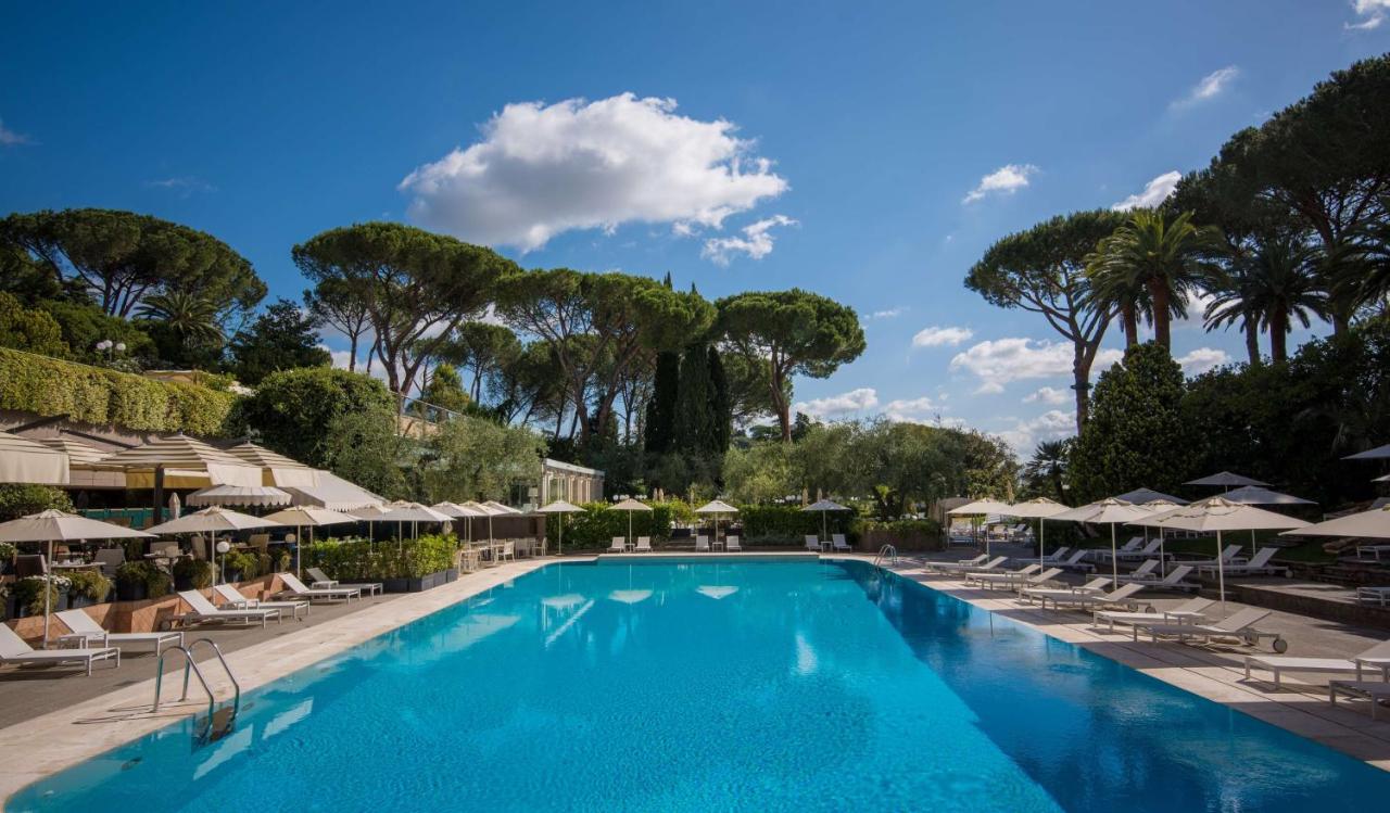 Large Hotel Rome Cavalieris pool with loungers and umbrellas, surrounded by lush tree canopies