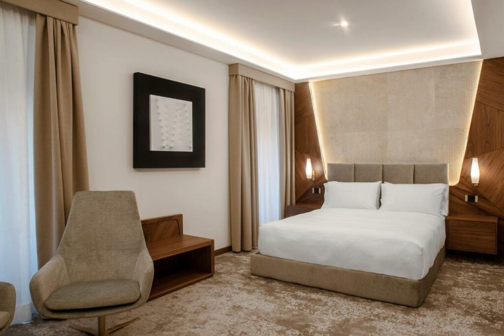 A cozy hotel room with a comfortable bed, a stylish chair, and warm lamps for a relaxing stay.